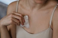 Close-up of a woman using a rose quartz gua sha stone on her chest for a relaxing beauty regimen.