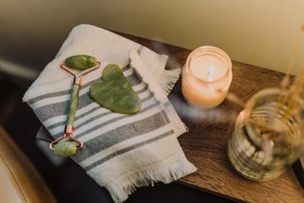Calming spa setup featuring a jade roller, gua sha stone, and candle for relaxation and skincare.